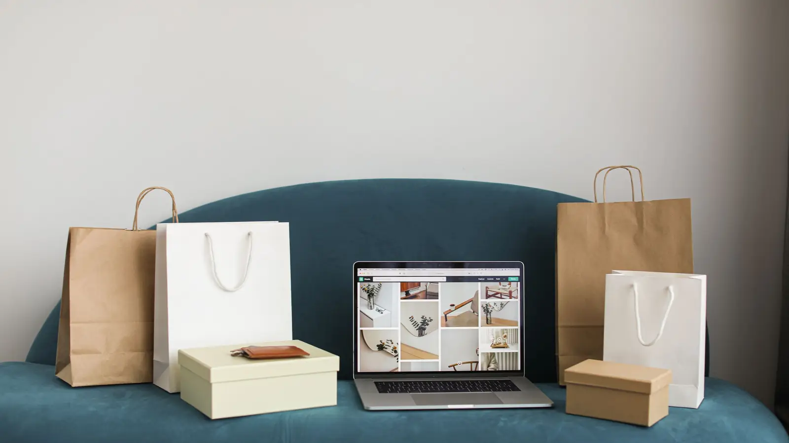 Laptop cu un magazin online deschis pe ecran, între pungi de cumpărături și cutii, pe o canapea