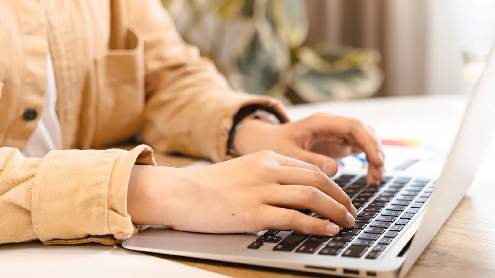 Mâini care tastează pe un laptop, pe un birou de lemn